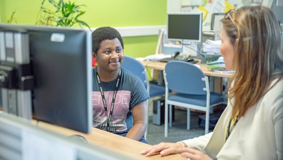 Male student sat at a desk with a computer on having a conversation with a female support tutor